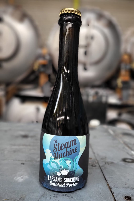 A bottle of Lapsang Souchong smoked porter beer from The Steam Machine, standing on a gray metal surface with a blurred industrial background.